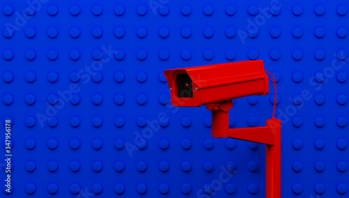 Red surveillance camera on blue background monitoring people on the street. Camera to search for quarantine offenders caused by Coronavirus