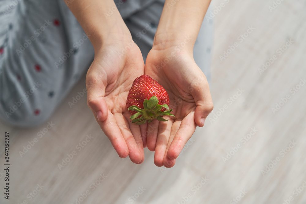 © PHILIPPE DEGROOTE/ADDICTIVE STOCK - From above top view of anonymous kid sitting on floor and demonstrating fresh strawberry on summer day at home © PHILIPPE DEGROOTE/ADDICTIVE STOCK - From above top view of anonymous kid sitting on floor and demonstrating fresh strawberry on summer day at home