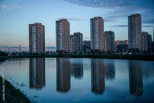 Beautiful view of the reflection of apartment buildings in a lake at sunset. Picturesque sky at sunset. © Алексей Васильев