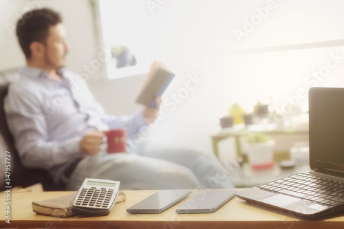 Man taking a break from work sitting in his living room reading a book and having a hot drink. Telecommuting, social media and gadget detoxification during quarantine. Digital detox.