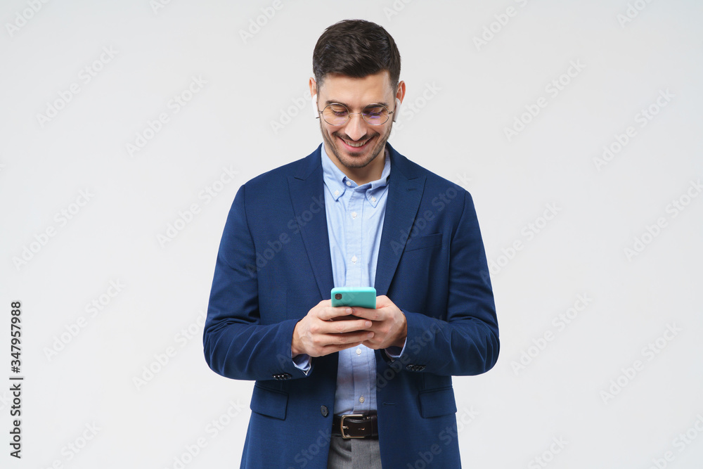 Young business man dressed in blazer and shirt, looking happily at screen of phone he is holding, reading funny messages, isolated on gray background Young business man dressed in blazer and shirt, looking happily at screen of phone he is holding, reading funny messages, isolated on gray background