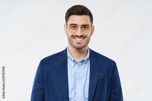 Young businessman wearing blue jacket, shirt and glasses, standing in front of camera, smiling happily, feeling confident, isolated on white background