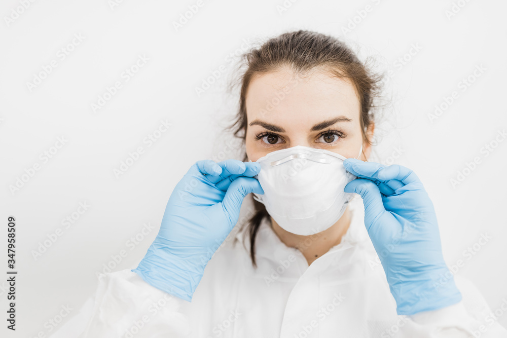The girl doctor puts on a white protective medical mask in blue gloves on a white background. The girl doctor puts on a white protective medical mask in blue gloves on a white background.