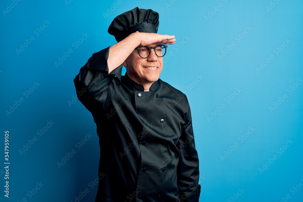 Middle age handsome grey-haired chef man wearing cooker uniform and hat very happy and smiling looking far away with hand over head. Searching concept. Middle age handsome grey-haired chef man wearing cooker uniform and hat very happy and smiling looking far away with hand over head. Searching concept.