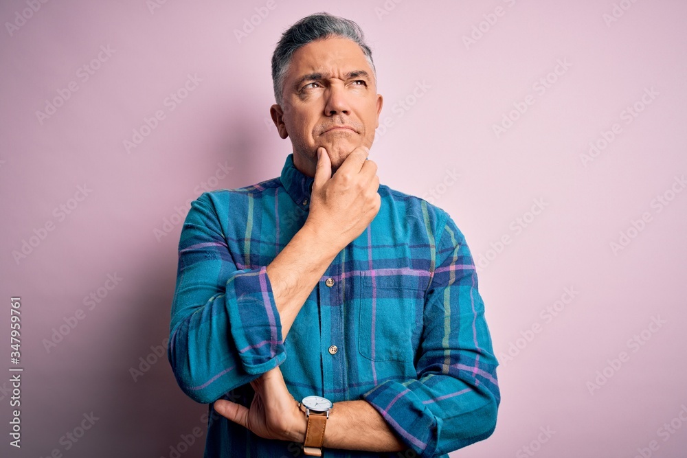 Middle age handsome grey-haired man wearing casual shirt over isolated pink background with hand on chin thinking about question, pensive expression. Smiling with thoughtful face. Doubt concept. Middle age handsome grey-haired man wearing casual shirt over isolated pink background with hand on chin thinking about question, pensive expression. Smiling with thoughtful face. Doubt concept.