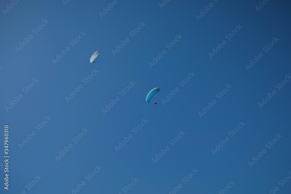 Two skydivers parachuting in the bright blue sky, looking up from below Two skydivers parachuting in the bright blue sky, looking up from below