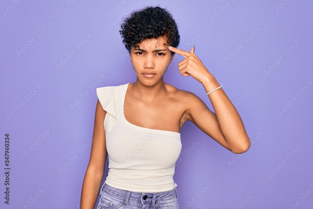 Young beautiful african american afro woman wearing casual t-shirt over purple background pointing unhappy to pimple on forehead, ugly infection of blackhead. Acne and skin problem Young beautiful african american afro woman wearing casual t-shirt over purple background pointing unhappy to pimple on forehead, ugly infection of blackhead. Acne and skin problem