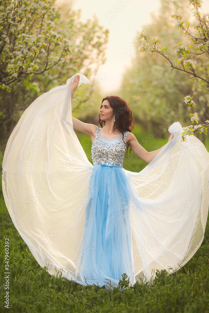 Portrait of beautiful curly brunette woman in trees blossoms garden. Wave evening dress. Portrait of beautiful curly brunette woman in trees blossoms garden. Wave evening dress.