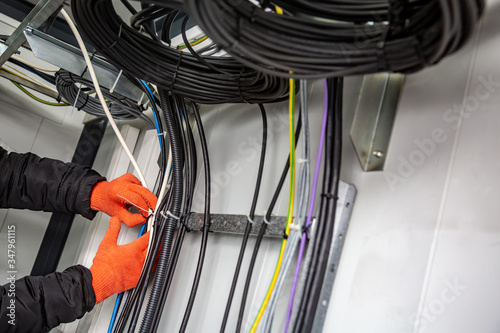 Hands with gloves fasten the cable ties on the cable, which are on the cable tray. Horizontal orientation.