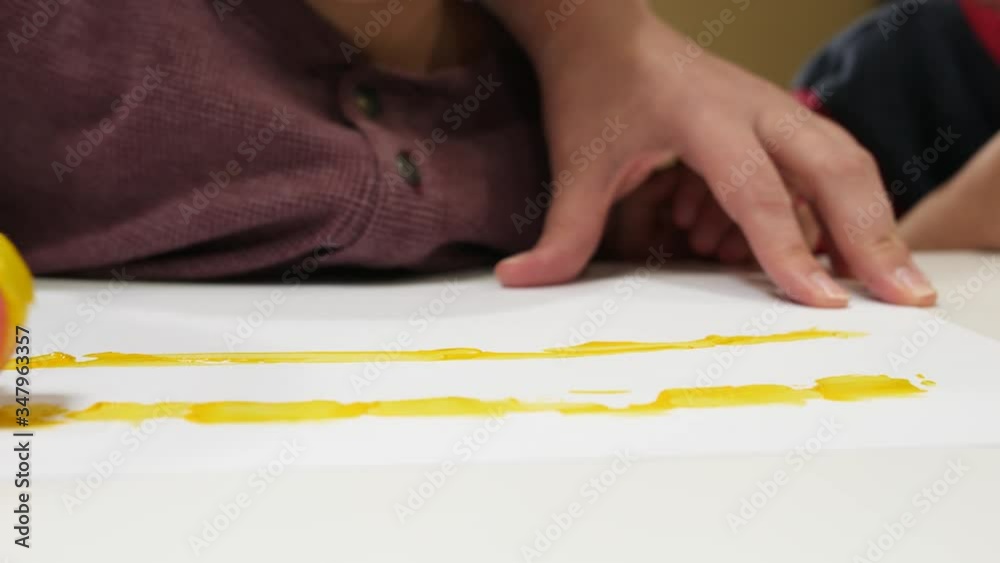 Painting Yellow on Paper Using a Sponge Roller. Hand held video as mom helps her kids to use a sponge roller.