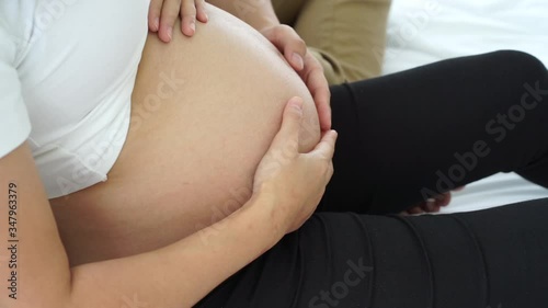 the young asian pregnancy woman with  husband sitting on the white bed with the hands touching the bally with love and care  photo