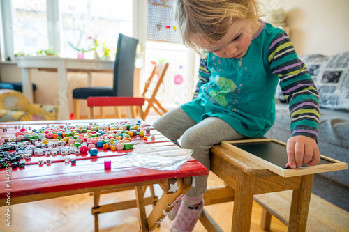 Cute girl playing with alpahbet beads and putting them on small black board.