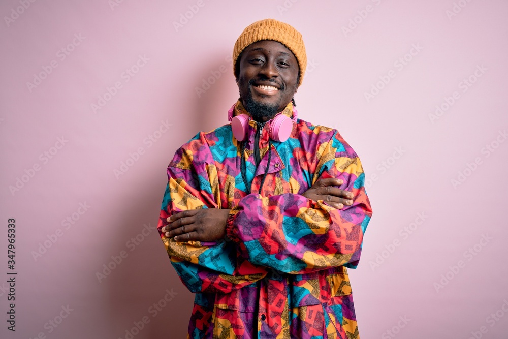 Young handsome african american man wearing colorful coat and cap over pink background happy face smiling with crossed arms looking at the camera. Positive person. Young handsome african american man wearing colorful coat and cap over pink background happy face smiling with crossed arms looking at the camera. Positive person.