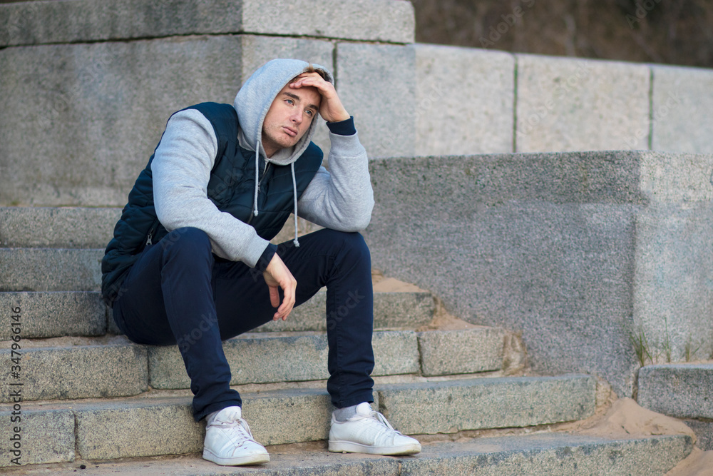 Unhappy sad upset depressed guy, young lonely frustrated man sitting on stairs in hood, suffering because of bad mood, thinking about future problems. Broken heart, failure concept. Unhappy sad upset depressed guy, young lonely frustrated man sitting on stairs in hood, suffering because of bad mood, thinking about future problems. Broken heart, failure concept.