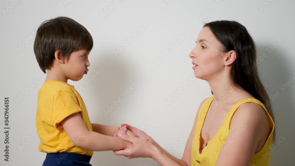 mother with her son a child of three years in yellow t-shirts, stands against a white wall in the studio and wants to kiss her mother with her son a child of three years in yellow t-shirts, stands against a white wall in the studio and wants to kiss her