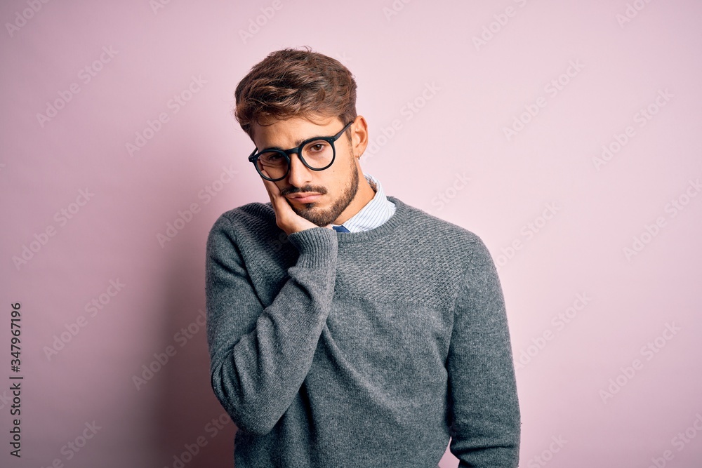 Young handsome man with beard wearing glasses and sweater standing over pink background thinking looking tired and bored with depression problems with crossed arms. Young handsome man with beard wearing glasses and sweater standing over pink background thinking looking tired and bored with depression problems with crossed arms.