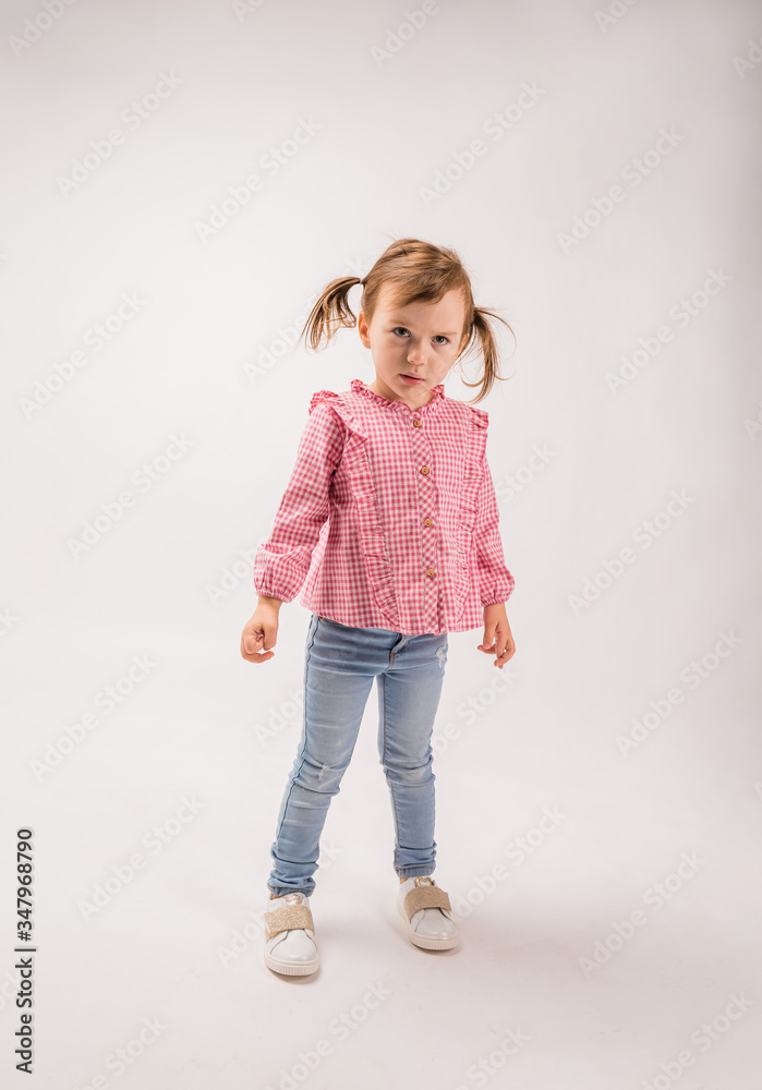 Angry little girl on a white background with copy space. Full-length portrait. A small aggressive girl in a plaid shirt and jeans stands on a white background. Angry little girl on a white background with copy space. Full-length portrait. A small aggressive girl in a plaid shirt and jeans stands on a white background.