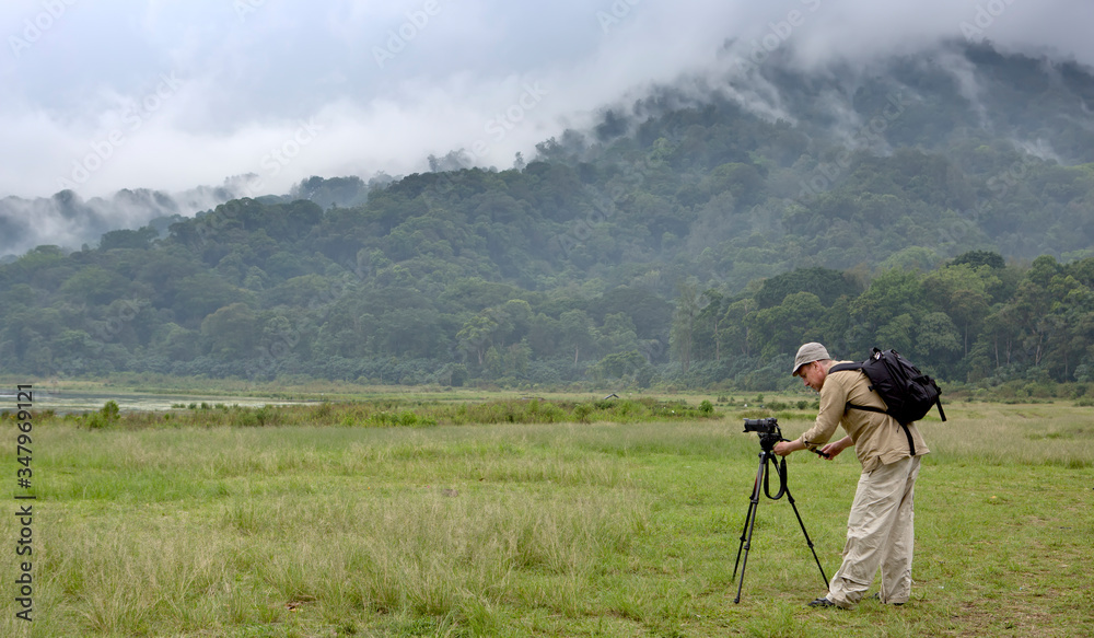 man with a camera on a tripod on a background of a mountain with a tropical forest. Bali. Indonesia.