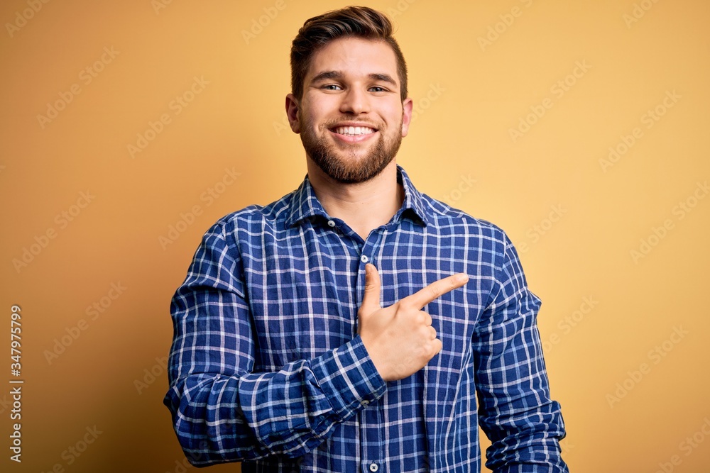 Young blond businessman with beard and blue eyes wearing shirt over yellow background cheerful with a smile on face pointing with hand and finger up to the side with happy and natural expression Young blond businessman with beard and blue eyes wearing shirt over yellow background cheerful with a smile on face pointing with hand and finger up to the side with happy and natural expression