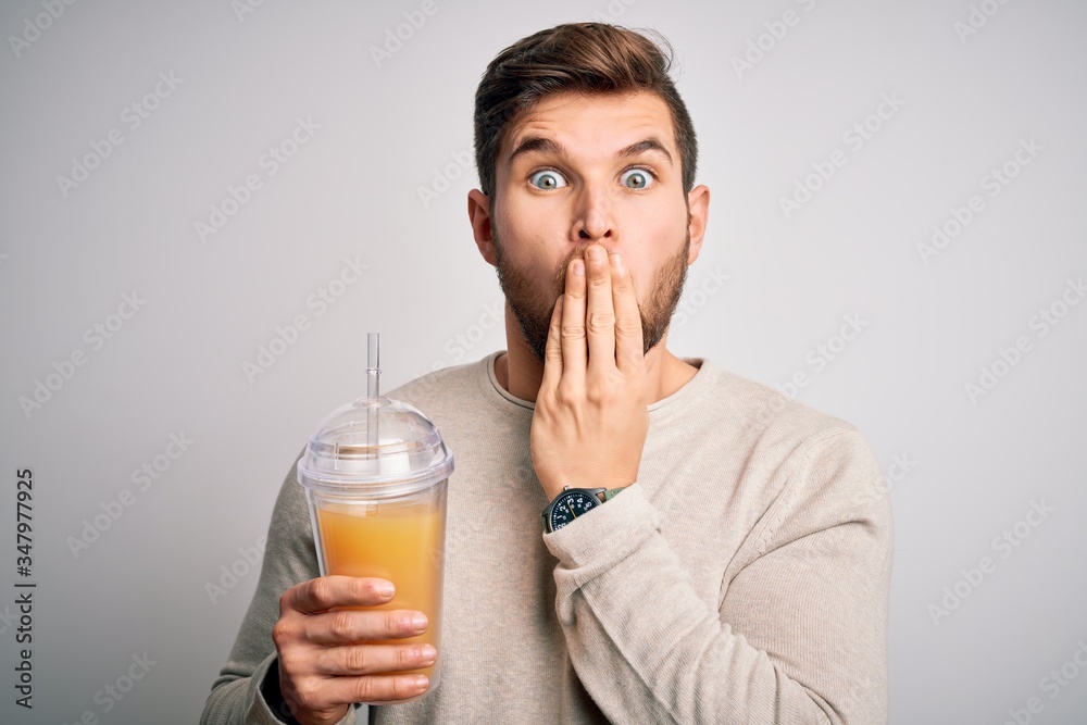 Young blond man with beard and blue eyes drinking healthy orange smoothie cover mouth with hand shocked with shame for mistake, expression of fear, scared in silence, secret concept Young blond man with beard and blue eyes drinking healthy orange smoothie cover mouth with hand shocked with shame for mistake, expression of fear, scared in silence, secret concept