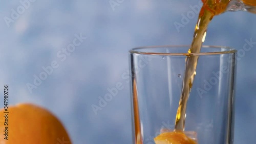 Yellow orange lemonade is poured into a clear glass with orange and ice. Slow motion.
