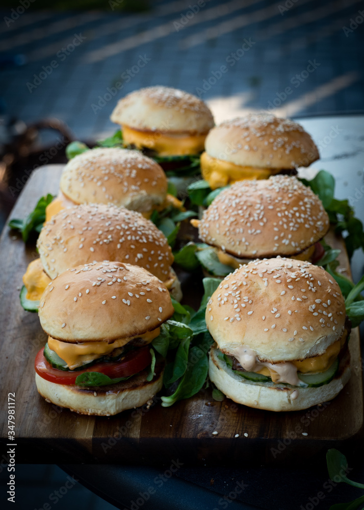 Closeup of fresh burgers with molten cheese on a wooden plate Closeup of fresh burgers with molten cheese on a wooden plate