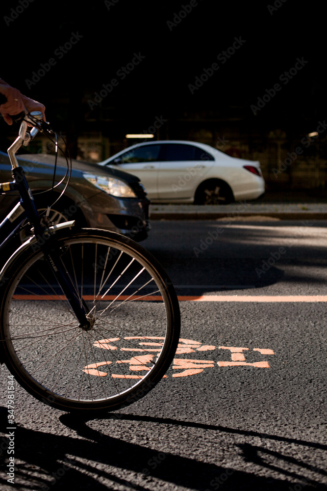 Cycle lane with orange painted bike on asphalt. Bicycle lane and car traffic. Ecological green urban transport. Fahrradspur und Autoverkehr. Fahrrad Zeichen auf Straße. Ökologischer urbaner Verkehr.