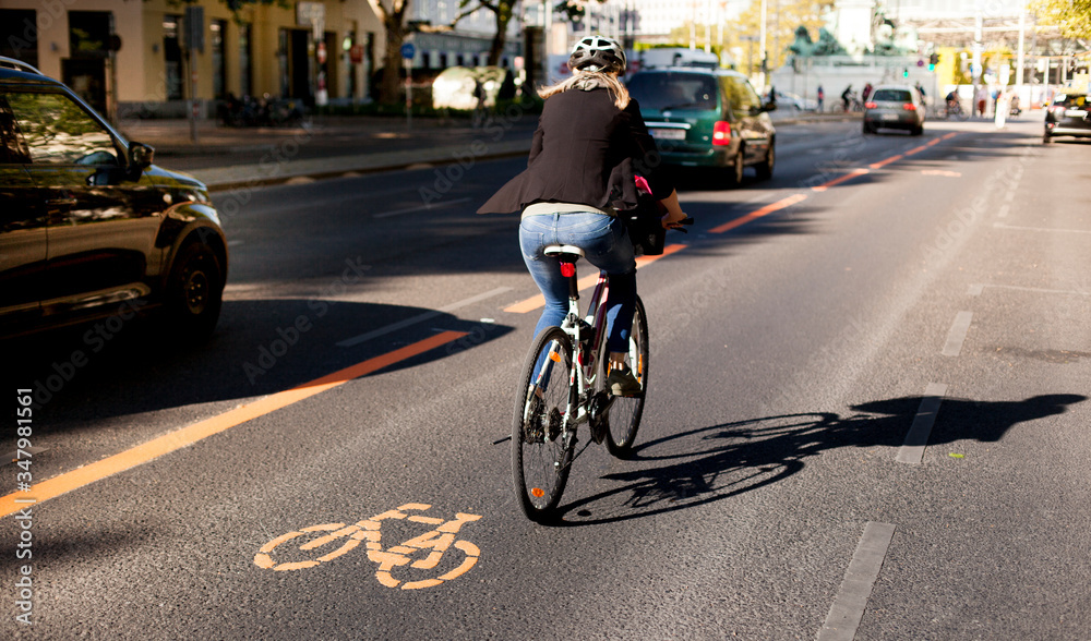 Cycle lane with orange painted bike on asphalt. Bicycle lane and car traffic. Ecological green urban transport. Fahrradspur und Autoverkehr. Fahrrad Zeichen auf Straße. Ökologischer urbaner Verkehr. - obrazy, fototapety, plakaty 