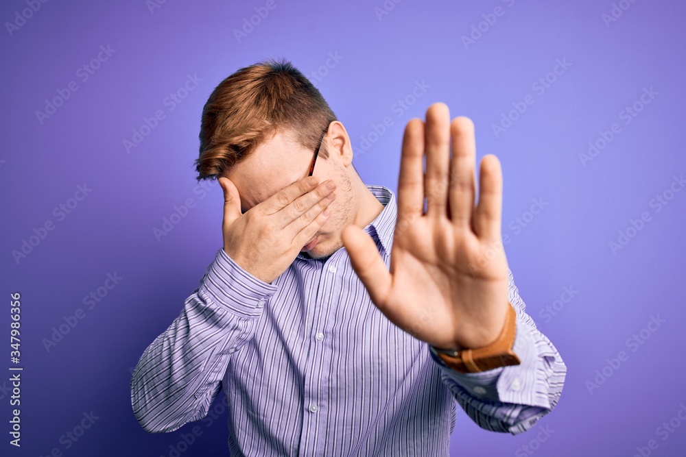 Young handsome redhead man wearing casual shirt and glasses over purple background covering eyes with hands and doing stop gesture with sad and fear expression. Embarrassed and negative concept. Young handsome redhead man wearing casual shirt and glasses over purple background covering eyes with hands and doing stop gesture with sad and fear expression. Embarrassed and negative concept.