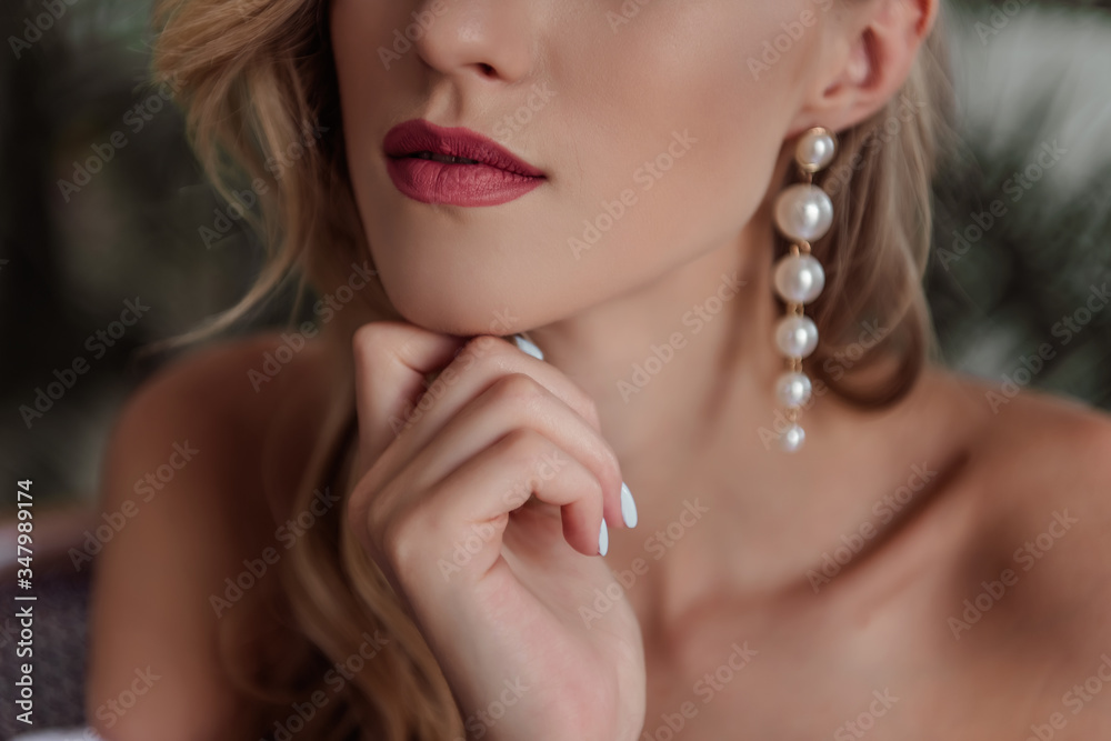 A beautiful girl with natural, beautiful, professional makeup and a fancy fashion fashion cut in her hair and long white pearl earrings. hands near the face, a large portrait. selective focus