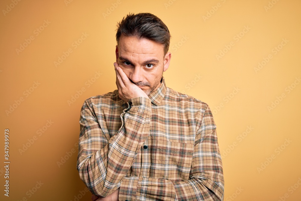 Young handsome man wearing casual shirt standing over isolated yellow background thinking looking tired and bored with depression problems with crossed arms.