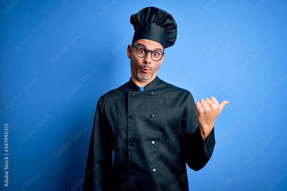Young handsome chef man wearing cooker uniform and hat over isolated blue background Surprised pointing with hand finger to the side, open mouth amazed expression. Young handsome chef man wearing cooker uniform and hat over isolated blue background Surprised pointing with hand finger to the side, open mouth amazed expression.