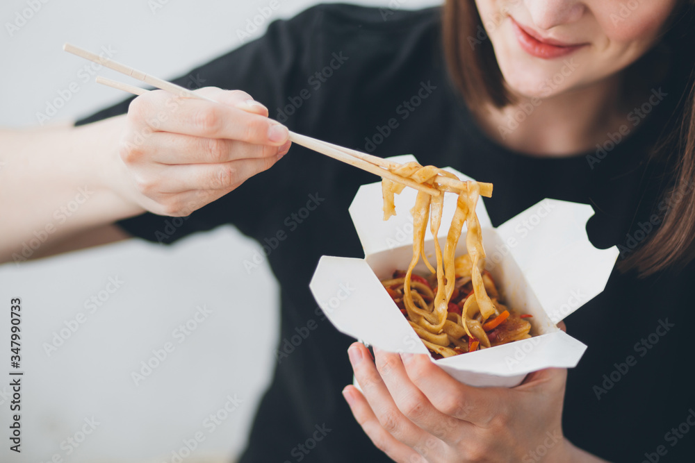 Woman eating asian chineese food noodles with vegetables in wok box using chopsticks. Food delivery. Take away lunch.