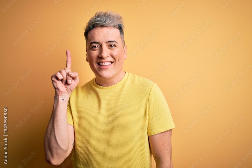 Young handsome modern man wearing yellow shirt over yellow isolated background showing and pointing up with finger number one while smiling confident and happy. Young handsome modern man wearing yellow shirt over yellow isolated background showing and pointing up with finger number one while smiling confident and happy.