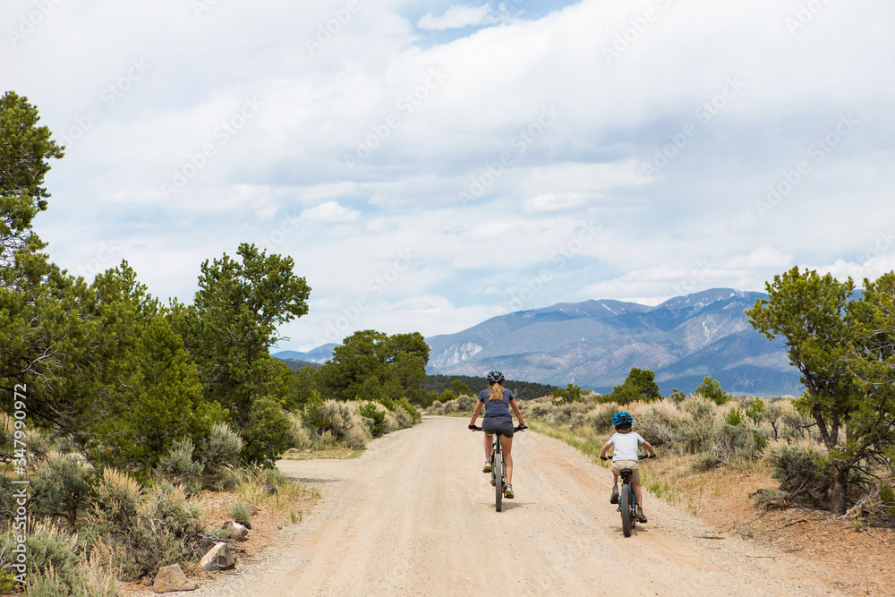 rear view of mother and young son on mountain bikes biking down dirt road rear view of mother and young son on mountain bikes biking down dirt road