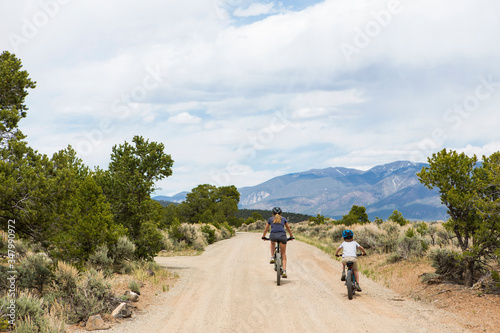 rear view of mother and young son on mountain bikes biking down dirt road photo