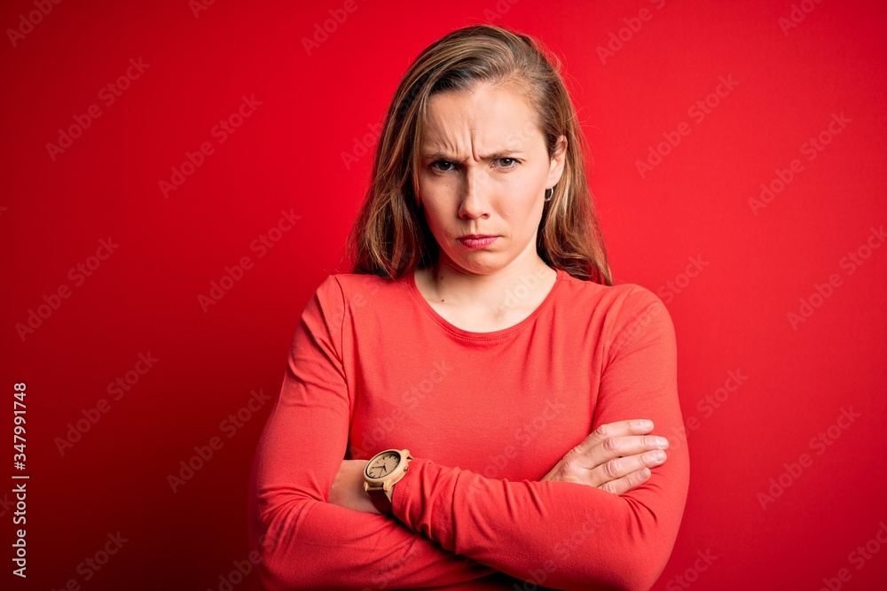 Obraz premium Young beautiful blonde woman wearing casual t-shirt standing over isolated red background skeptic and nervous, disapproving expression on face with crossed arms. Negative person.