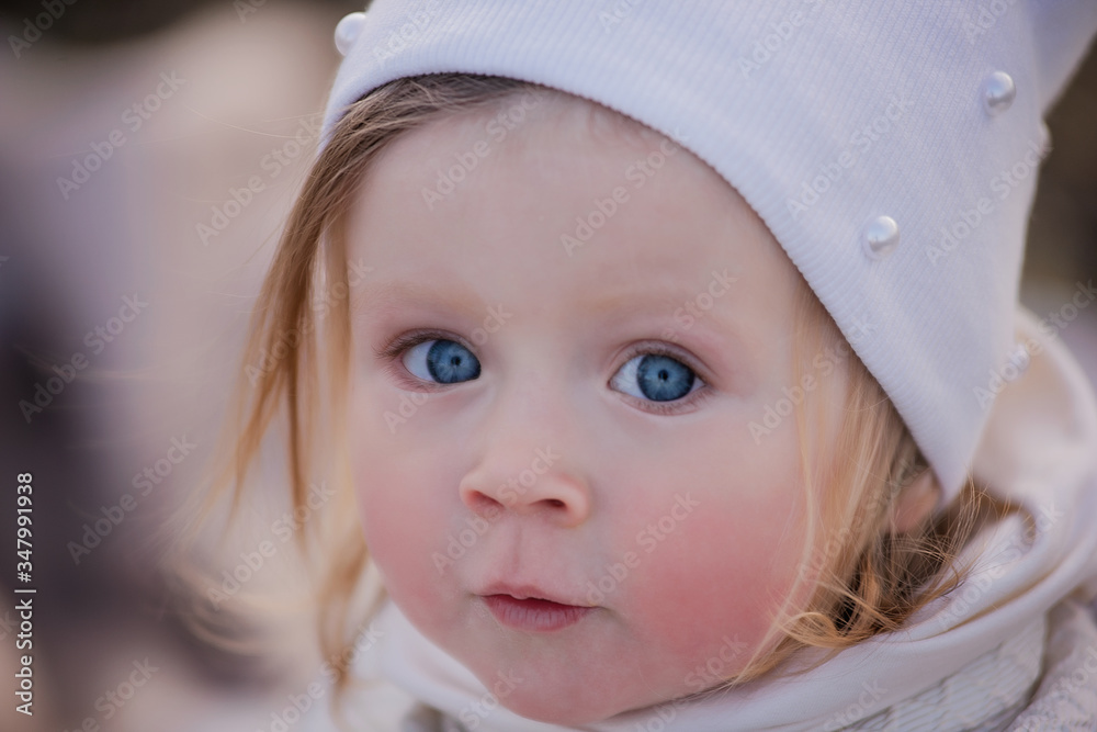 A large portrait of a beautiful little girl in a white hat with expressive big blue eyes. happy childhood - selective front and back focus A large portrait of a beautiful little girl in a white hat with expressive big blue eyes. happy childhood - selective front and back focus