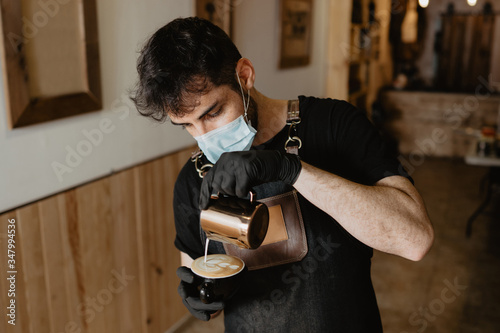 Barista con mascarilla y guantes de protección para antivirus realizando latte art en una taza de café photo