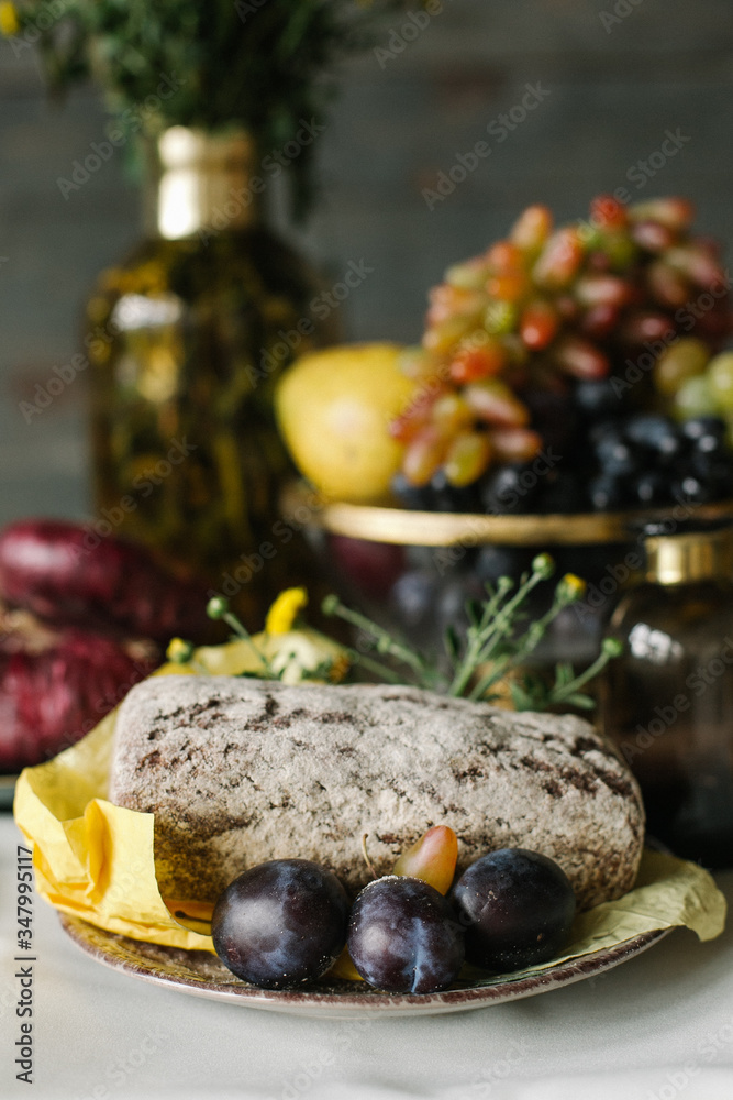 warm bread from the oven on a plate with plums and next to it is a vase of grapes warm bread from the oven on a plate with plums and next to it is a vase of grapes