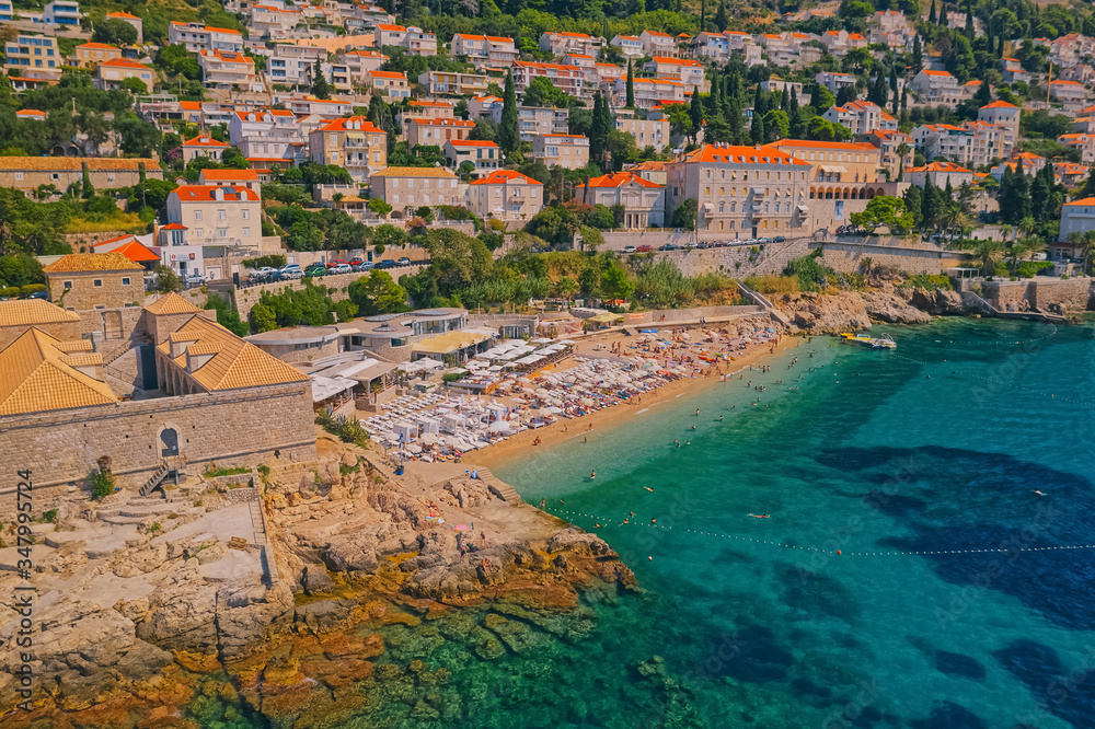 DUBROVNIK, CROATIA - AUGUST 28 2019: Aerial morning panorama of the famous beach Banje right next to the wall olf the old town Lazareti building