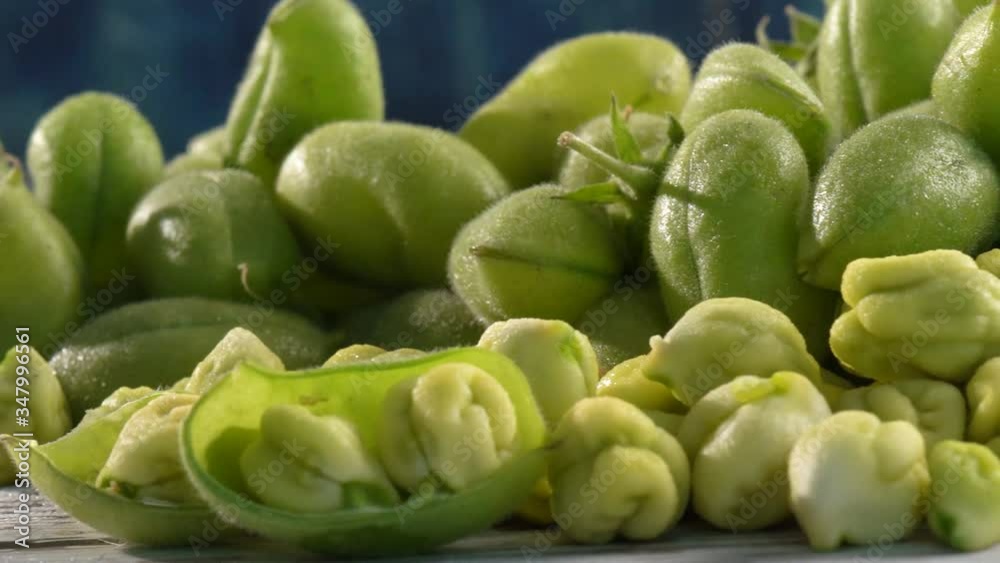Extreme closeup slider to the right of moist, raw, uncooked chickpeas in and out of their husk on a white rustic table with blue background. Extreme closeup slider to the right of moist, raw, uncooked chickpeas in and out of their husk on a white rustic table with blue background.