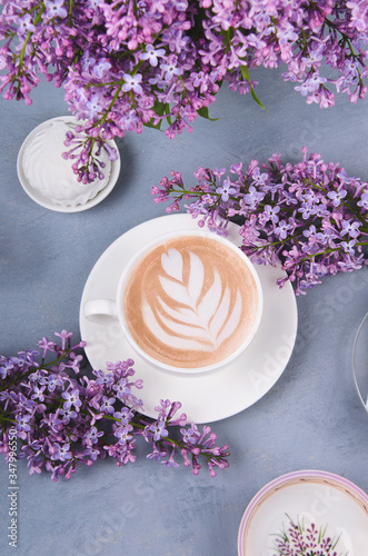Lilac, coffee with latte art and marshmallow on gray wooden table. Romantic morning. Flat lay
