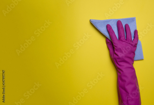 Hand in a pink (yellow) household glove with  rag wipes on colorfiul background. Professional sanitization against viruses and germs. Cleaning, desinfection concept. photo