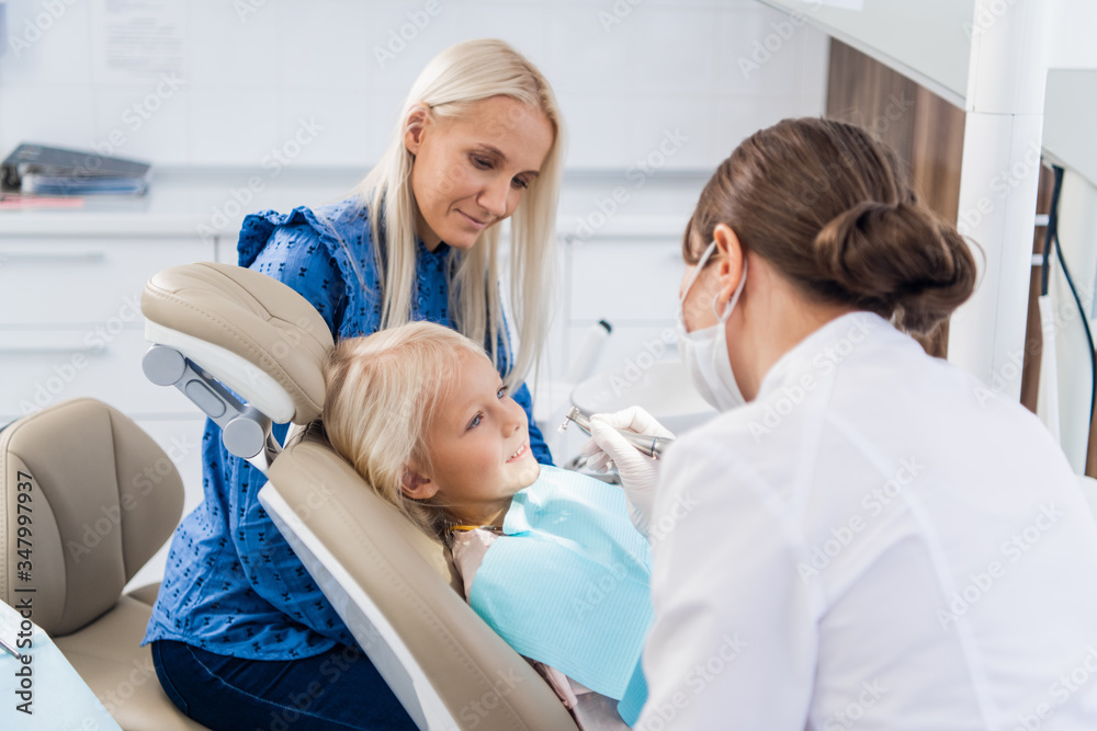 The dentist cleaning the girl's teeth with a special tool, the girl is looking at the doctor The dentist cleaning the girl's teeth with a special tool, the girl is looking at the doctor
