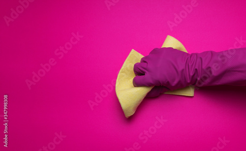 Hand in a pink (yellow) household glove with  rag wipes on colorfiul background. Professional sanitization against viruses and germs. Cleaning, desinfection concept. photo