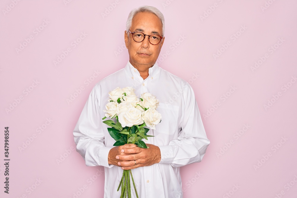 Middle age senior grey-haired man holding romantic bouquet of white roses over pink background with a confident expression on smart face thinking serious Middle age senior grey-haired man holding romantic bouquet of white roses over pink background with a confident expression on smart face thinking serious