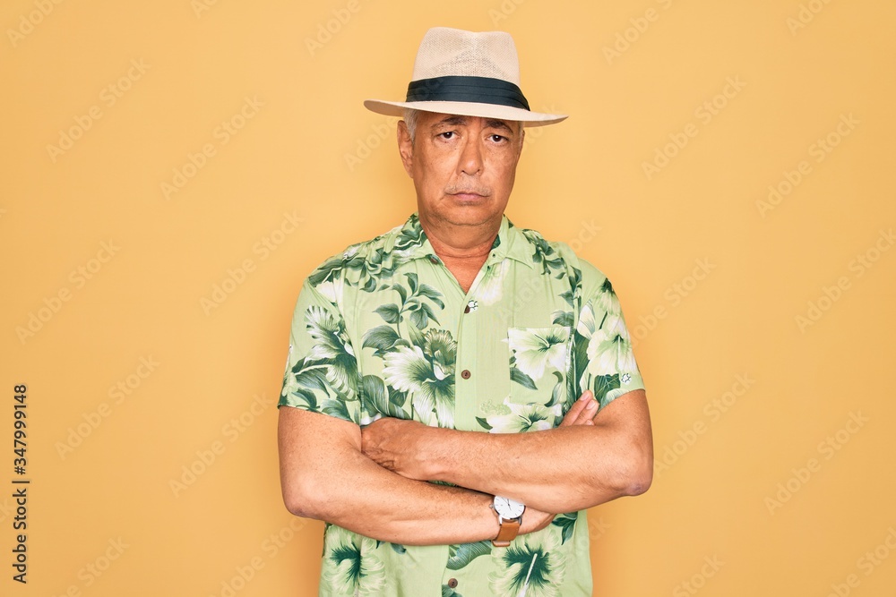 Middle age senior grey-haired man wearing summer hat and floral shirt on beach vacation skeptic and nervous, disapproving expression on face with crossed arms. Negative person.