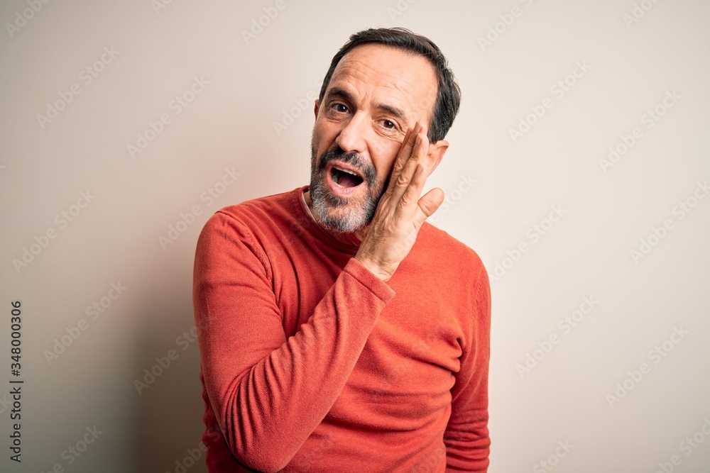 Middle age hoary man wearing casual orange sweater standing over isolated white background hand on mouth telling secret rumor, whispering malicious talk conversation Middle age hoary man wearing casual orange sweater standing over isolated white background hand on mouth telling secret rumor, whispering malicious talk conversation