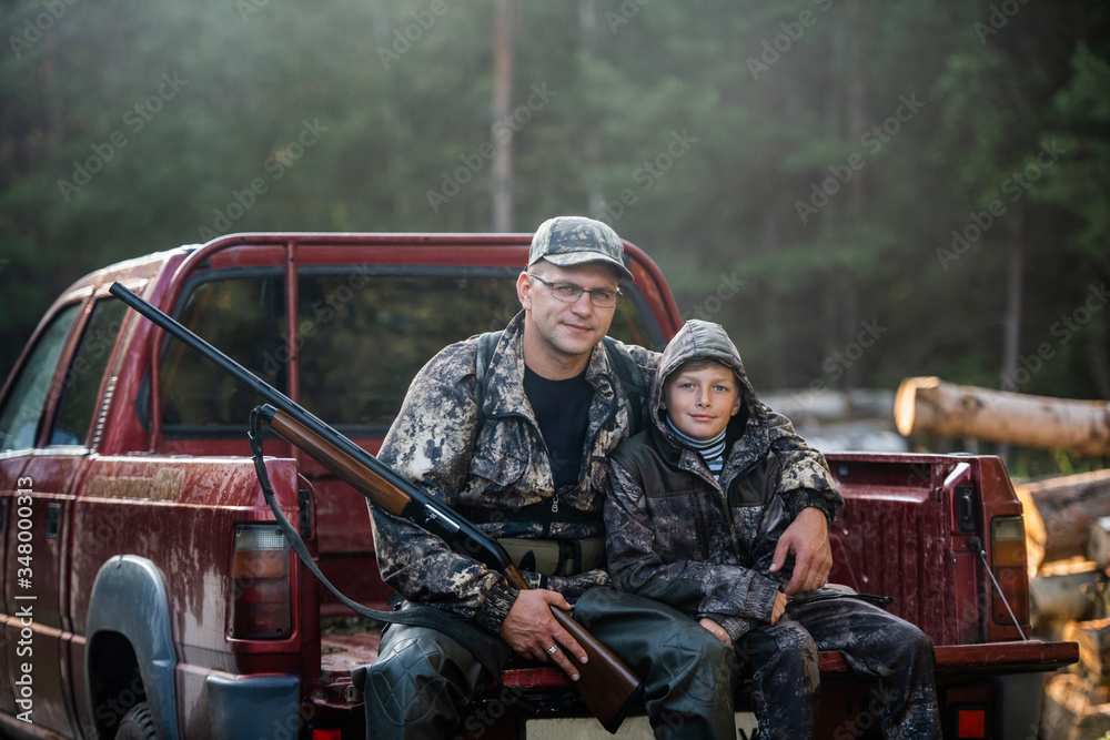 Fototapeta premium Father and son sitting in a pickup truck after hunting in forest. Dad showing boy mechanism of a shotgun rifle.